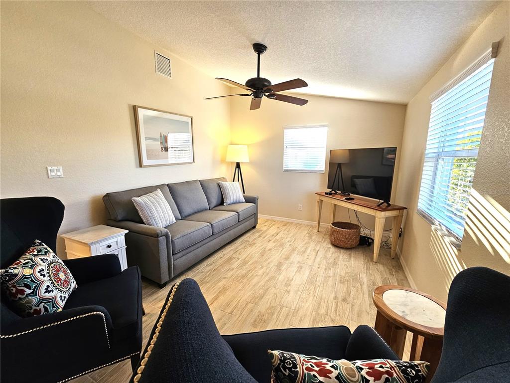 A living room features a gray sofa, two dark armchairs, a television, and wood-look flooring — 1153 CLARK STREET, ENGLEWOOD, FL
