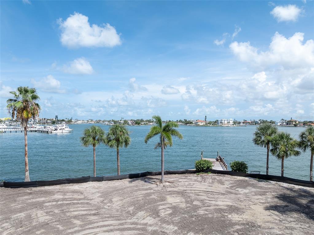 A vacant waterfront lot features palm trees, a small wooden dock, and a sandy surface — 1 PARADISE LANE, TREASURE ISLAND, FL