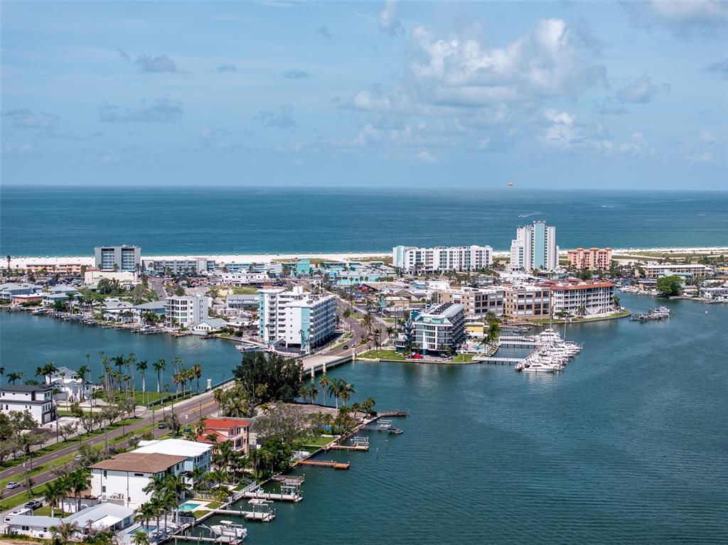 An aerial view shows a coastal town with buildings, a bridge, and boats on the water — 1 PARADISE LANE, TREASURE ISLAND, FL
