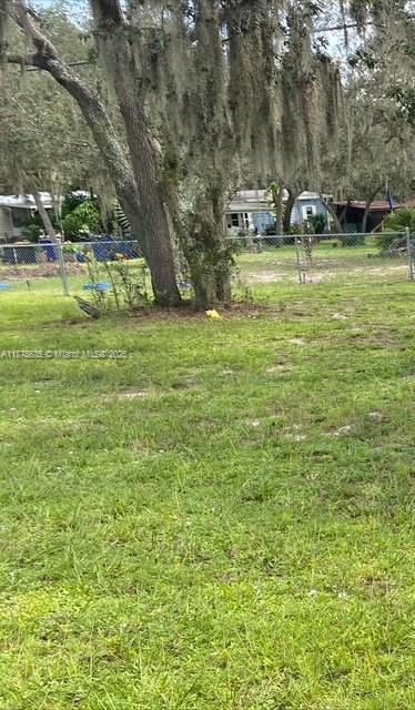 A grassy yard features a large tree draped in Spanish moss behind a chain-link fence — 6005 Lake Front Dr, Sebring FL 33876, SEBRING, FL