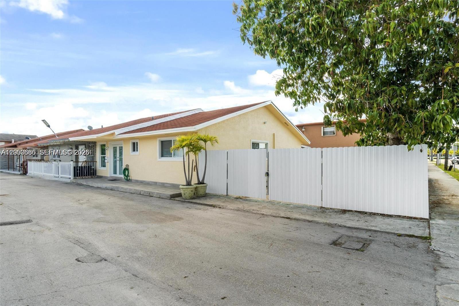A yellow single-story house features a white privacy fence and a paved driveway — 330 W 74th Pl # 330, Hialeah FL 33014, HIALEAH, FL