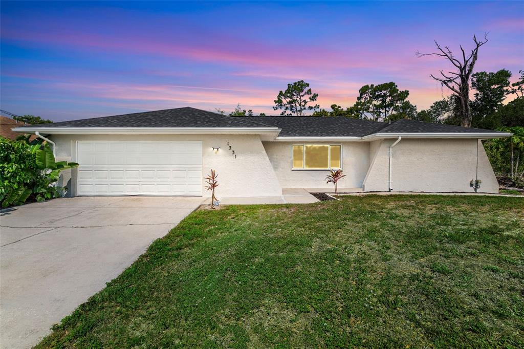 A single-story house with a white stucco exterior, a two-car garage, and a grassy lawn — 1231 BEACON DRIVE, PORT CHARLOTTE, FL