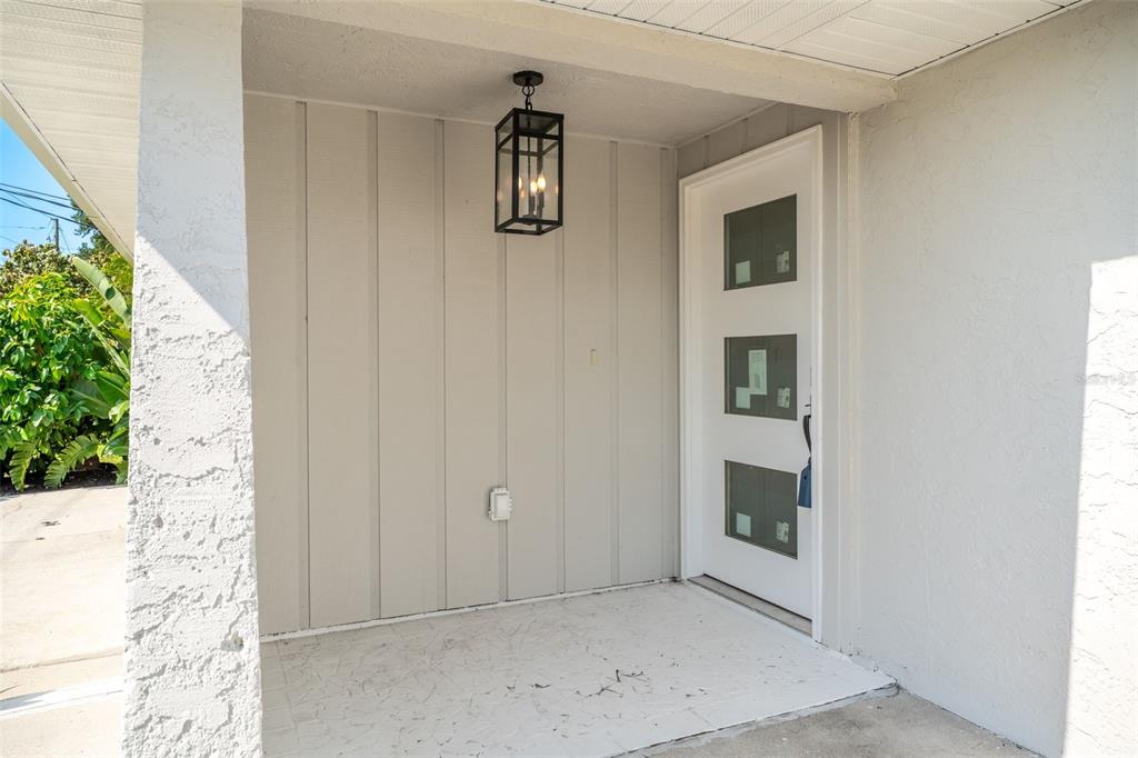 A covered entryway features a white door with three rectangular windows and a hanging lantern — 1231 BEACON DRIVE, PORT CHARLOTTE, FL