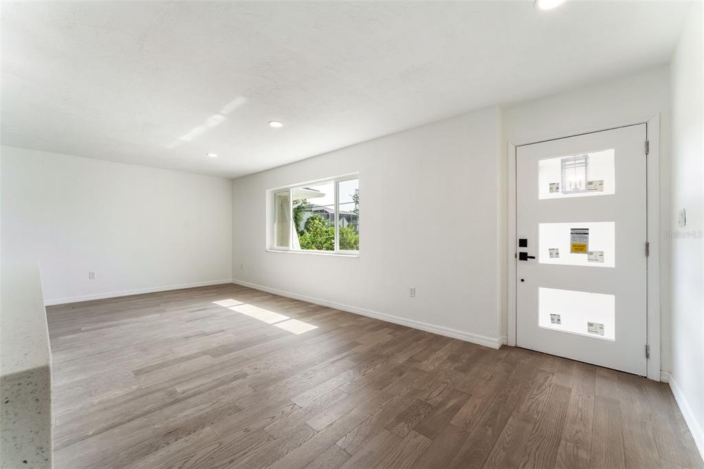 An empty room with light wood flooring, white walls, a window, and a white front door — 1231 BEACON DRIVE, PORT CHARLOTTE, FL