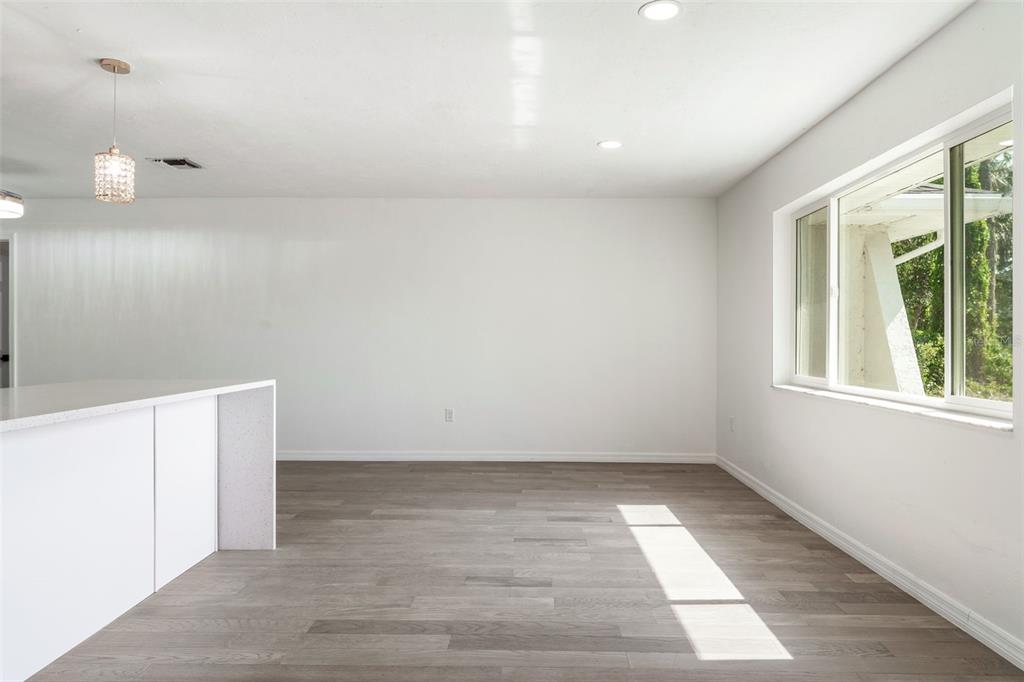 An empty room with white walls, gray wood-look flooring, a kitchen island, and large windows — 1231 BEACON DRIVE, PORT CHARLOTTE, FL