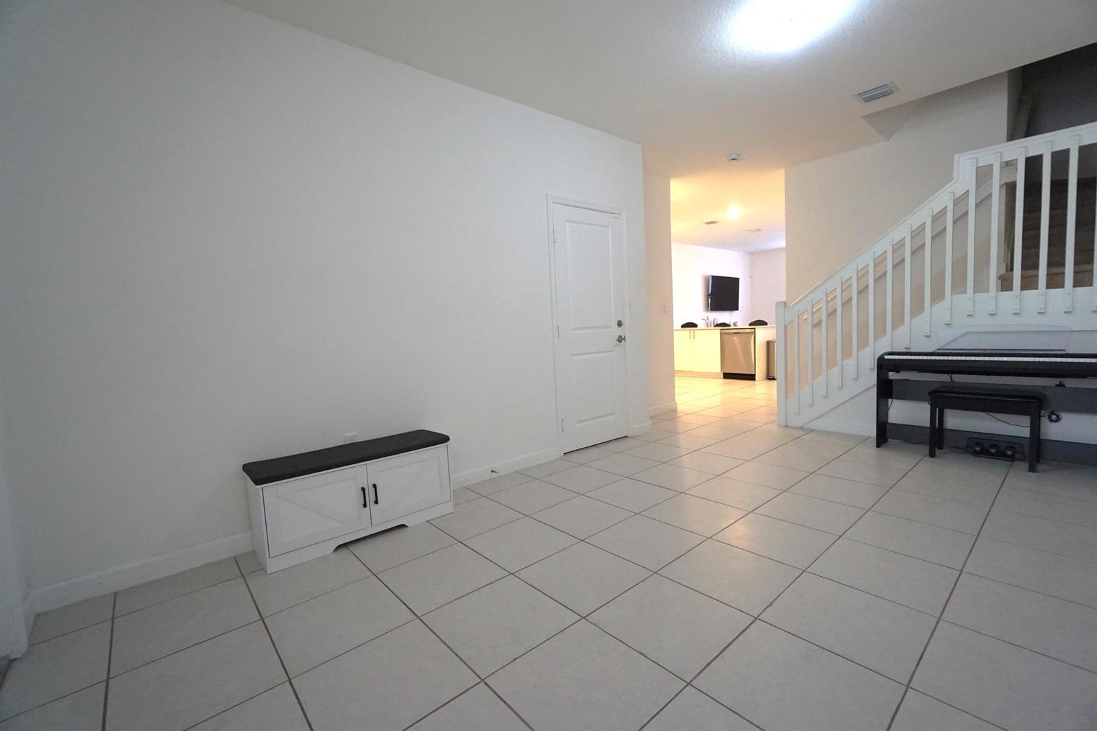 A tiled room features a white storage bench, a closed door, and a staircase — 23010 SW 128th Place, Miami FL 33170, MIAMI, FL