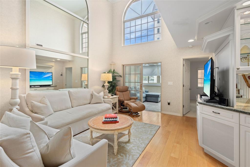 A living room features high ceilings, a large arched window, mirrored walls, and hardwood floors — 1161 COQUILLE STREET UNIT 206, SARASOTA, FL
