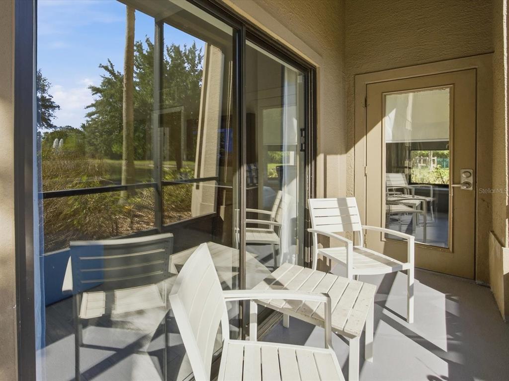 A covered patio features white slatted chairs, a small table, and a sliding glass door — 14501 GROVE RESORT AVENUE UNIT 1114, WINTER GARDEN, FL