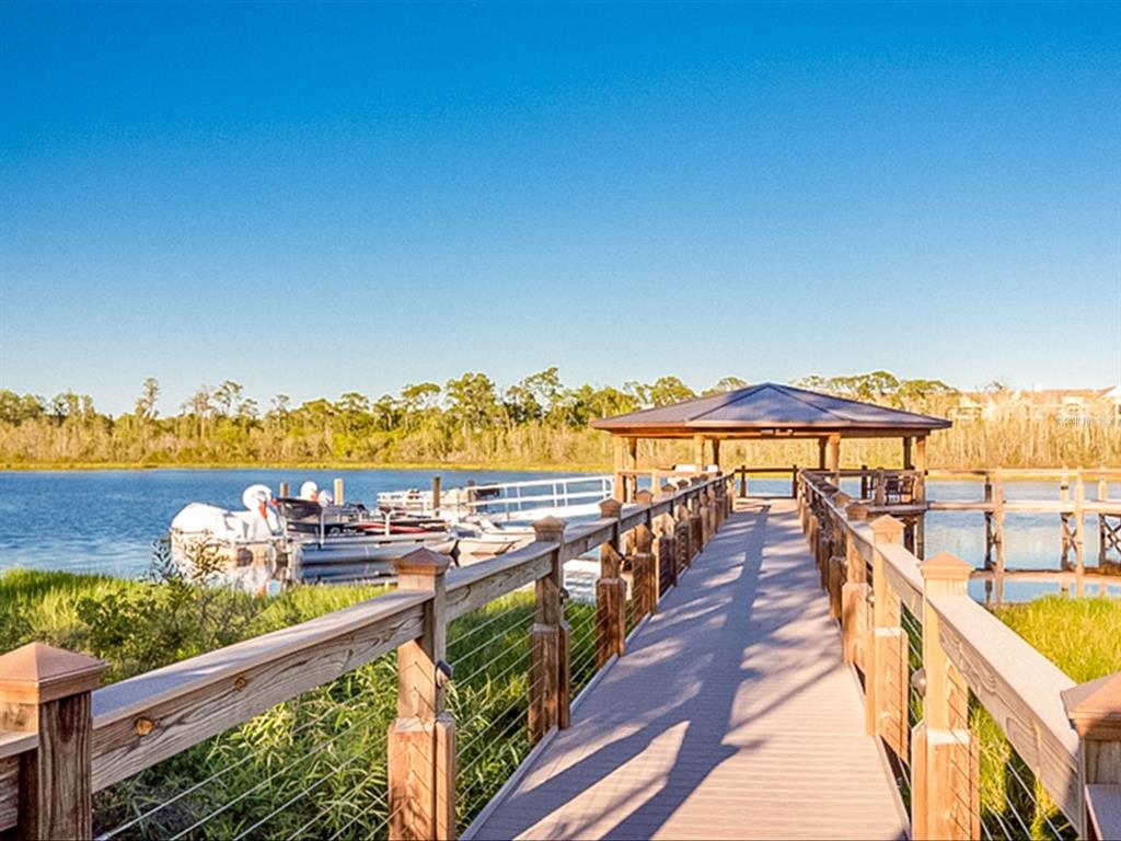 A wooden boardwalk leads to a covered gazebo on a lake with docked boats — 14501 GROVE RESORT AVENUE UNIT 1114, WINTER GARDEN, FL