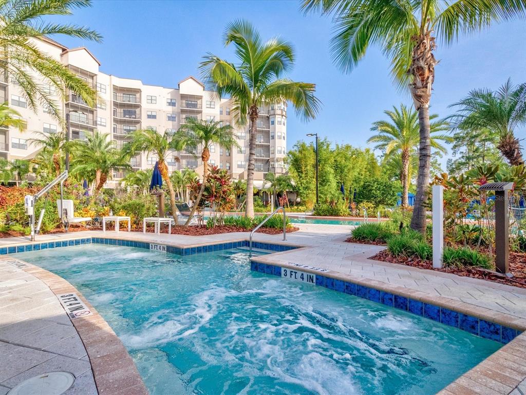 A bubbling hot tub sits on a paved pool deck surrounded by palm trees and landscaping — 14501 GROVE RESORT AVENUE UNIT 1114, WINTER GARDEN, FL