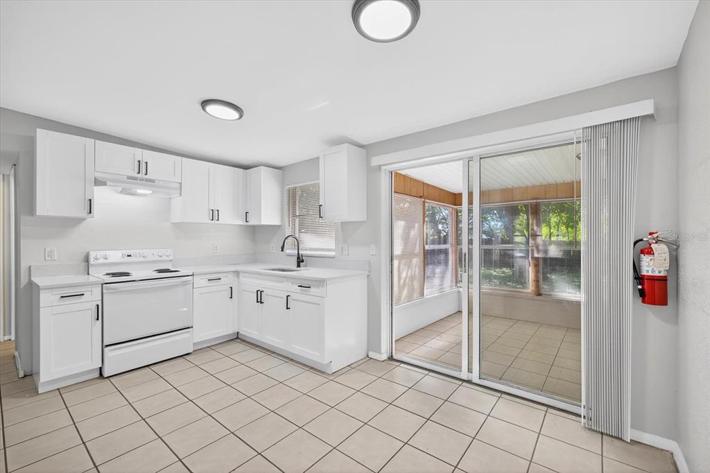 A kitchen with white cabinets, white appliances, and tile flooring next to a sliding door — 11015 MARTHA AVENUE, PORT RICHEY, FL
