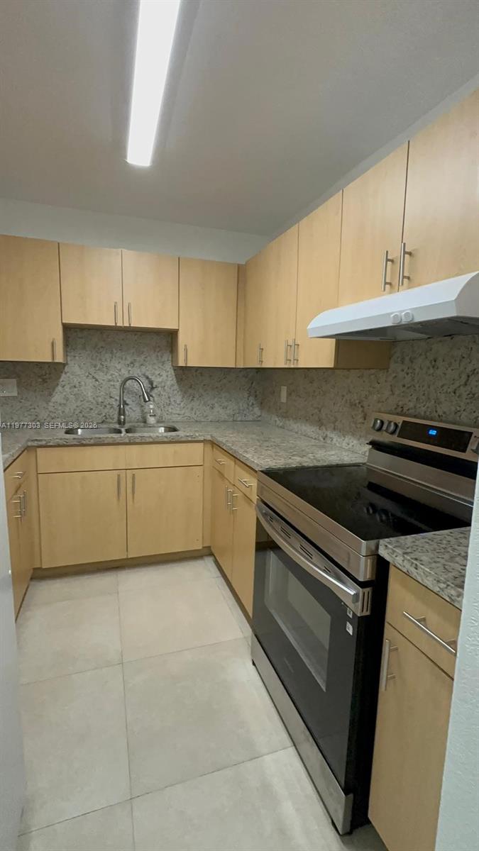 A kitchen features light wood cabinets, granite countertops, and stainless steel appliances — 1885 W 56th St # 112, Hialeah FL 33012, HIALEAH, FL
