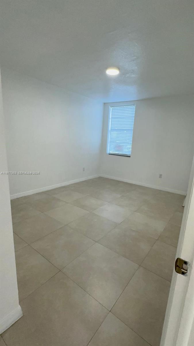 An empty room features white walls, light-colored tile flooring, and a single window with blinds — 1885 W 56th St # 112, Hialeah FL 33012, HIALEAH, FL