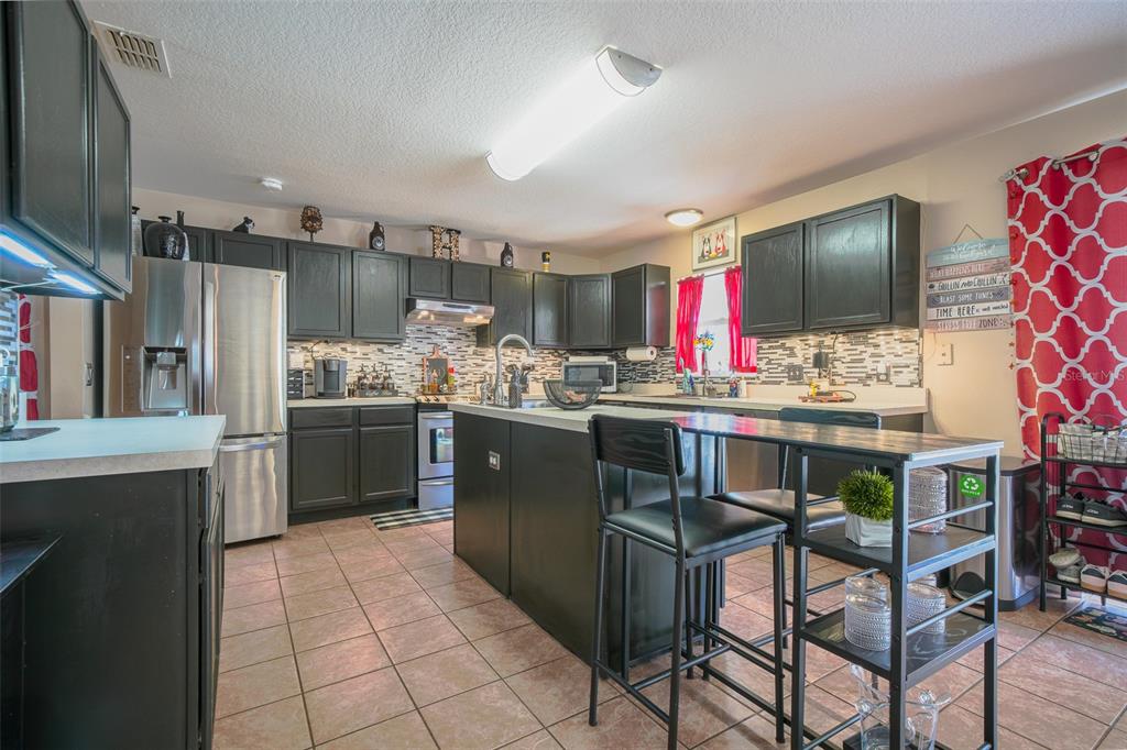 A kitchen features dark cabinets, stainless steel appliances, a central island, and tiled flooring — 613 LOBELIA DRIVE, DAVENPORT, FL