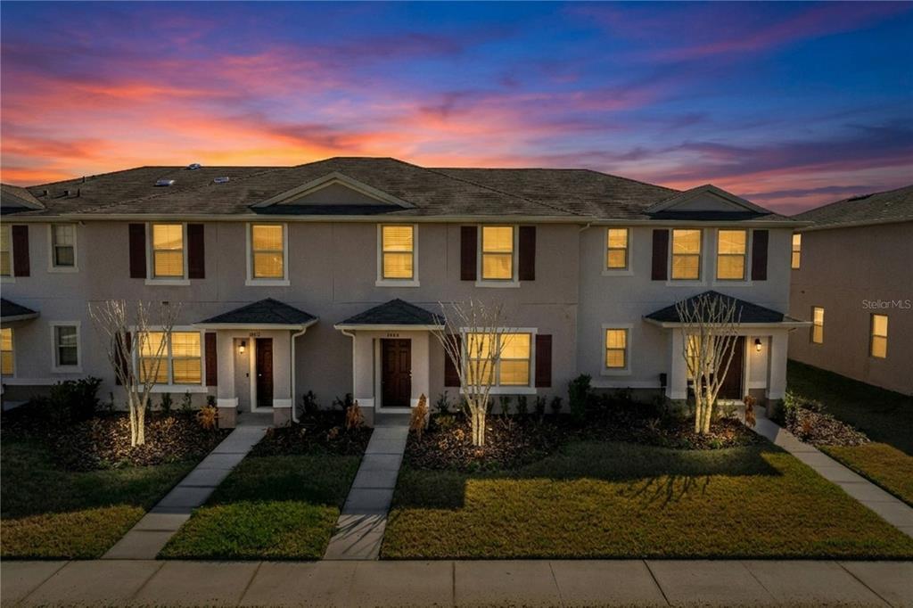 A multi-unit townhouse building features beige stucco siding, dark shutters, and small front porches at dusk — 1404 DUSTY STONE LANE, KISSIMMEE, FL
