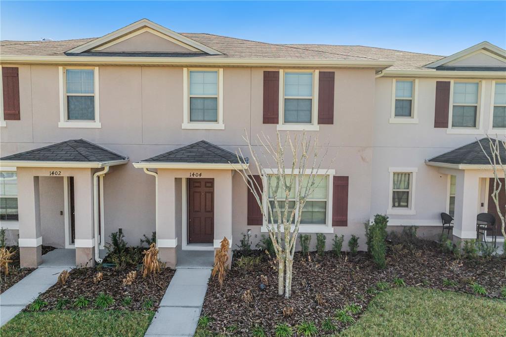 The exterior of a two-story townhouse features beige stucco walls, brown shutters, and covered entryways — 1404 DUSTY STONE LANE, KISSIMMEE, FL