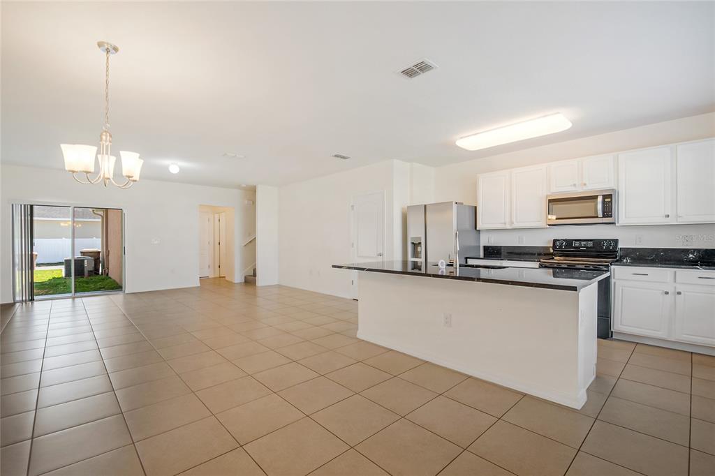 An open-concept kitchen and dining area features white cabinets, granite countertops, and tile flooring — 1404 DUSTY STONE LANE, KISSIMMEE, FL