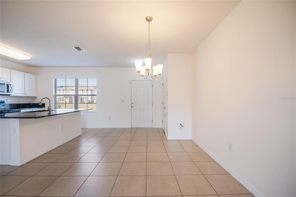 A dining area with tile flooring, a chandelier, and an adjacent kitchen with white cabinets — 1404 DUSTY STONE LANE, KISSIMMEE, FL