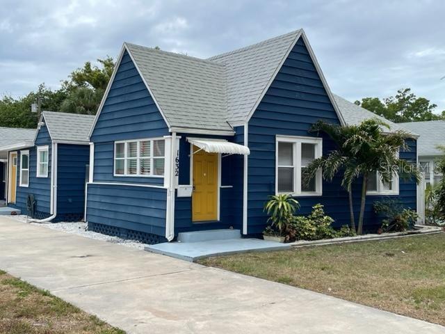 A blue house with a yellow front door and a concrete driveway under a cloudy sky — 1632 27TH AVENUE N, ST PETERSBURG, FL