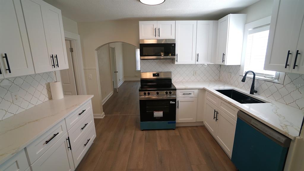 A renovated kitchen features white cabinets, stainless steel appliances, quartz countertops, and a tile backsplash — 1632 27TH AVENUE N, ST PETERSBURG, FL