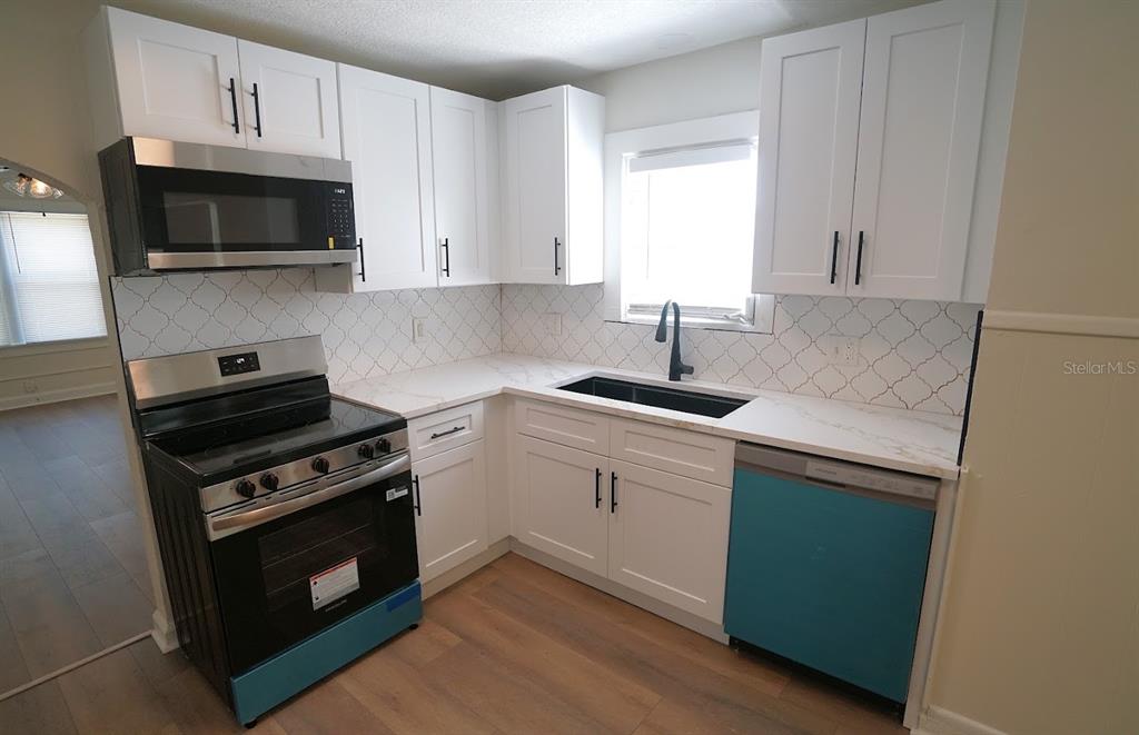 A kitchen features white cabinets, stainless steel appliances, a black sink, and patterned tile backsplash — 1632 27TH AVENUE N, ST PETERSBURG, FL