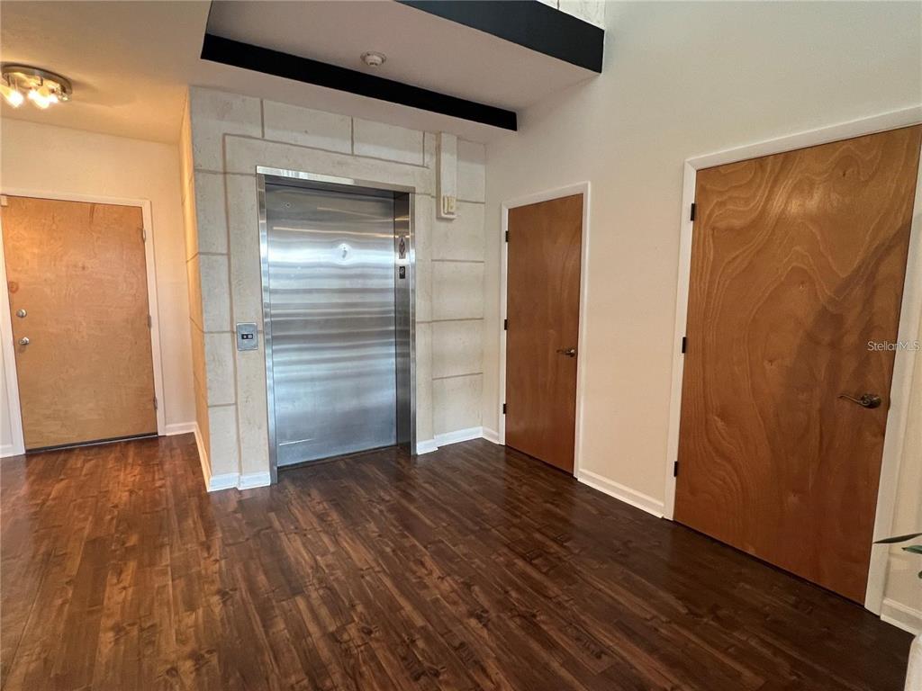 A room with wood flooring, three wooden doors, and a central stainless steel elevator — 101 PALM HARBOR PARKWAY UNIT A404, PALM COAST, FL