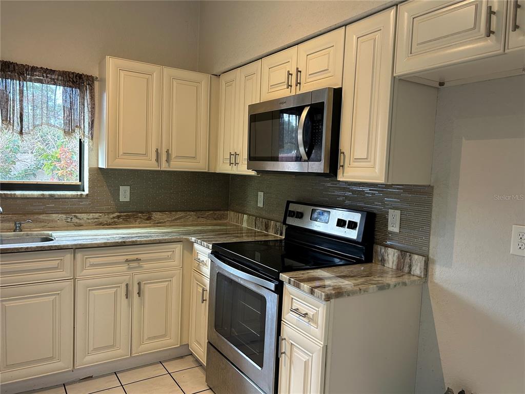 A kitchen features cream-colored cabinets, stainless steel appliances, and a brown tiled backsplash — 9814 PINEY POINT CIRCLE, ORLANDO, FL