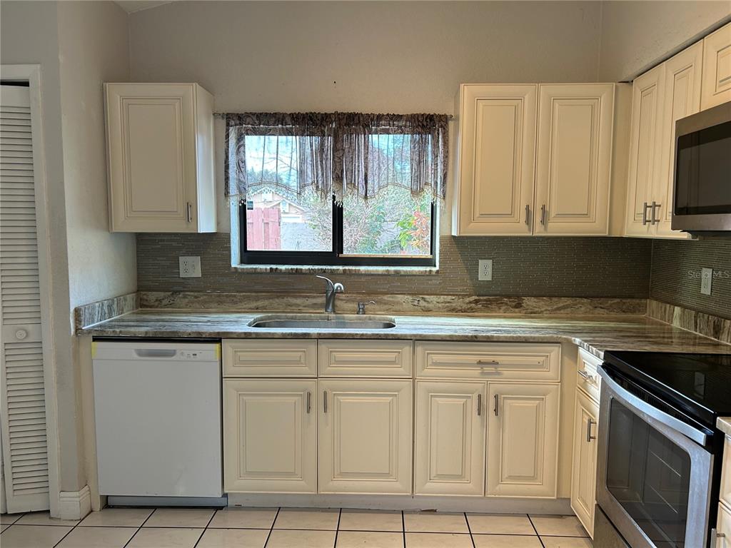 A kitchen features cream-colored cabinets, a stone-patterned countertop, a tiled backsplash, and stainless steel appliances — 9814 PINEY POINT CIRCLE, ORLANDO, FL