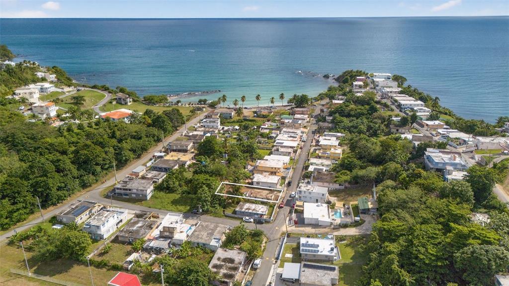 An aerial view shows a coastal neighborhood with a highlighted vacant lot near the ocean — COMM. HUCARES 119, NAGUABO, PR