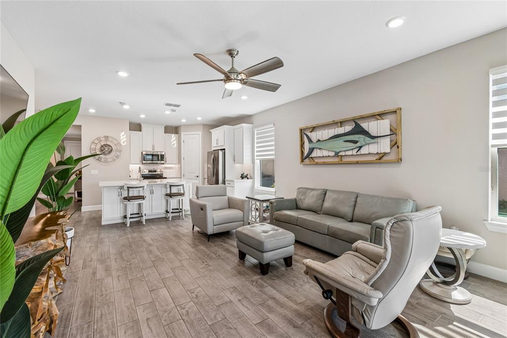 An open-concept living room and kitchen featuring light gray furniture, tile flooring, and white cabinetry — 779 VIA COMO ST, POINCIANA, FL