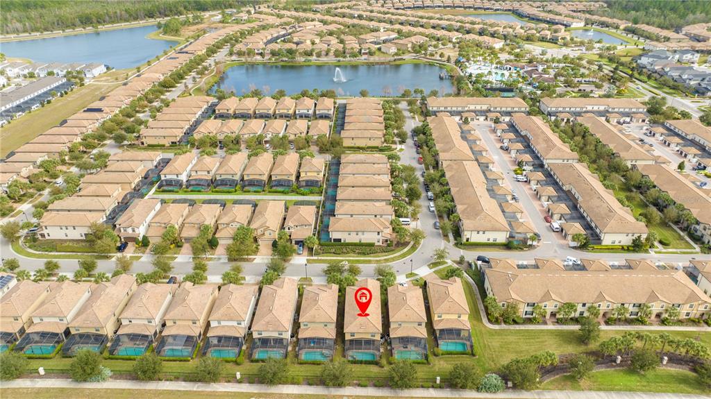 An aerial view shows a suburban neighborhood with townhomes, swimming pools, and a central lake — 9013 RHODES STREET, KISSIMMEE, FL