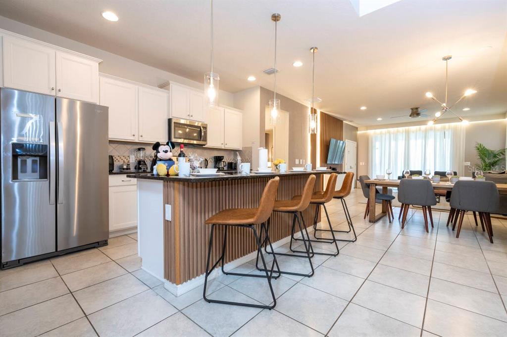A kitchen with white cabinets, stainless steel appliances, and a wood-paneled island with bar stools — 9013 RHODES STREET, KISSIMMEE, FL