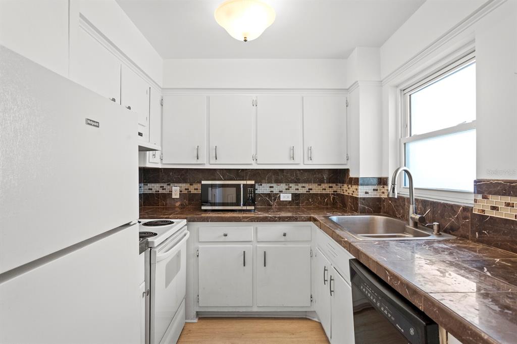 A kitchen features white cabinets, dark marble countertops, a tile backsplash, and white appliances — 750 BURLINGTON AVENUE N UNIT 3C, ST PETERSBURG, FL