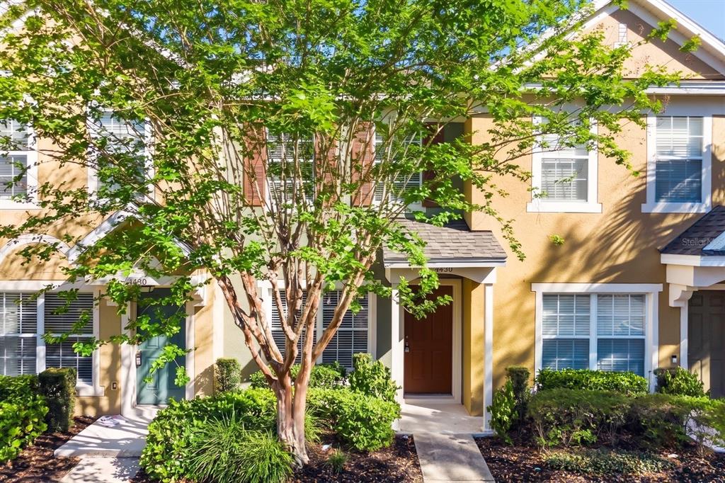 A two-story townhouse exterior with a central tree, brown front door, and tan siding — 1450 STOCKTON DRIVE, SANFORD, FL