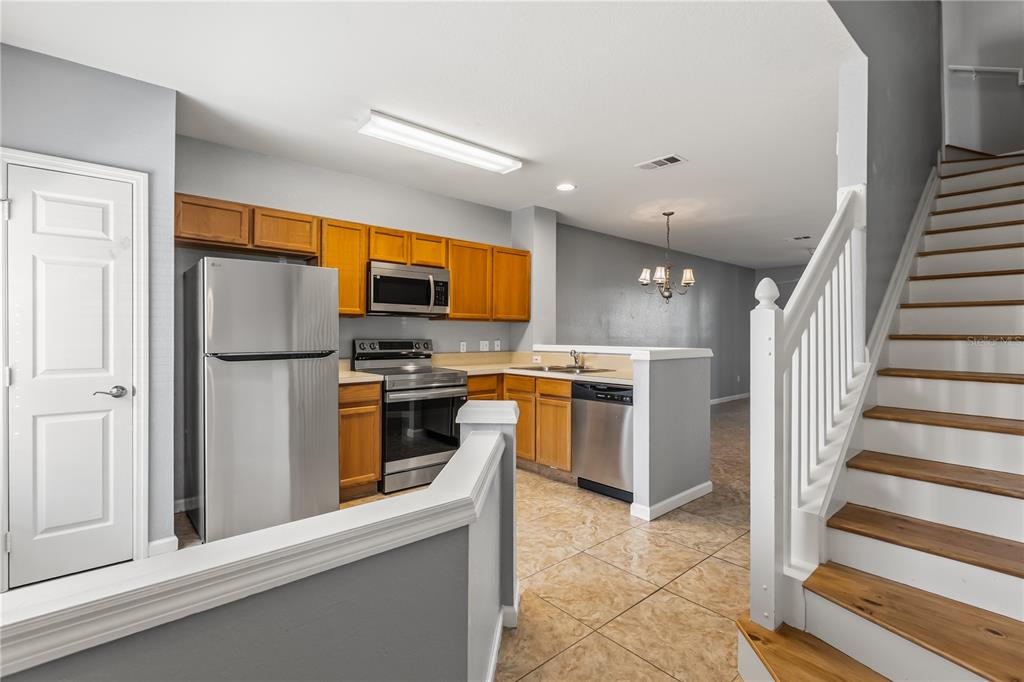 A kitchen with stainless steel appliances and wood cabinets sits beside a wooden staircase — 1450 STOCKTON DRIVE, SANFORD, FL