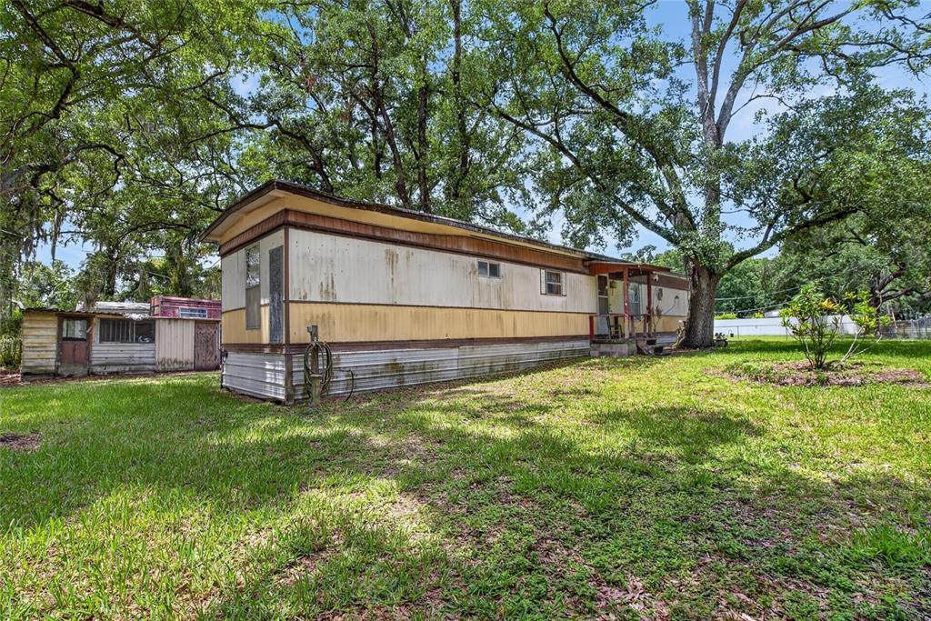 An older mobile home sits on a grassy lot shaded by large oak trees — 10227 OAK AVENUE, TAMPA, FL