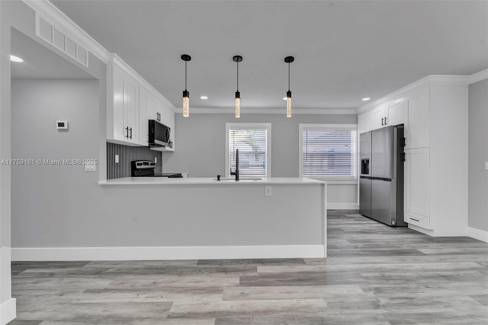 A modern kitchen features white cabinetry, stainless steel appliances, and gray wood-look flooring — 38 Flanders A # 38, Delray Beach FL 33484, DELRAY BEACH, FL