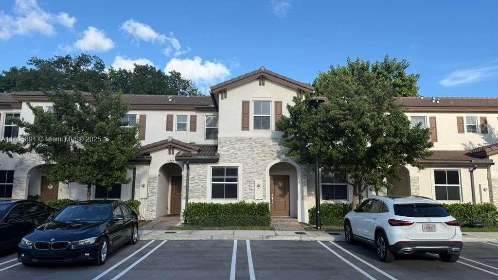 A two-story townhouse exterior features a stone facade, brown shutters, and two parked cars — 12445 NW 23rd Ct, Miami FL 33167, MIAMI, FL