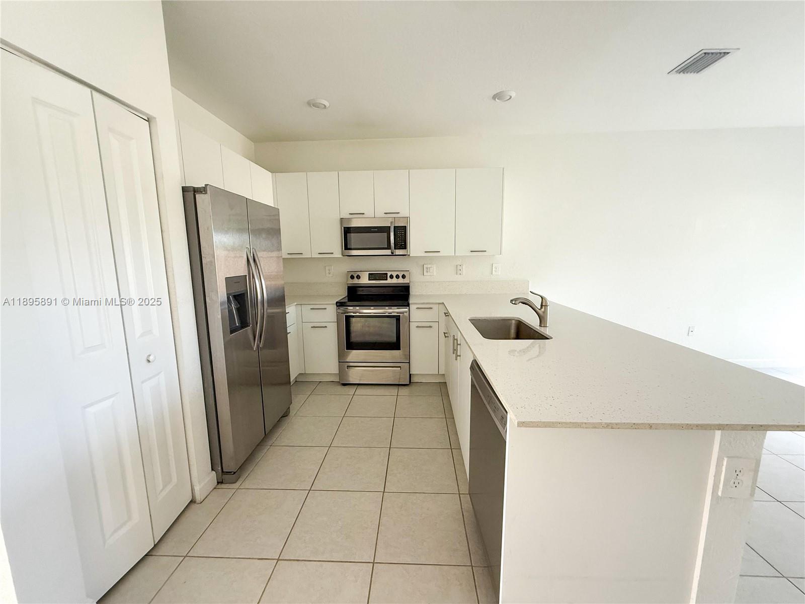 A kitchen features white cabinets, stainless steel appliances, and a quartz-topped island with a sink — 12445 NW 23rd Ct, Miami FL 33167, MIAMI, FL