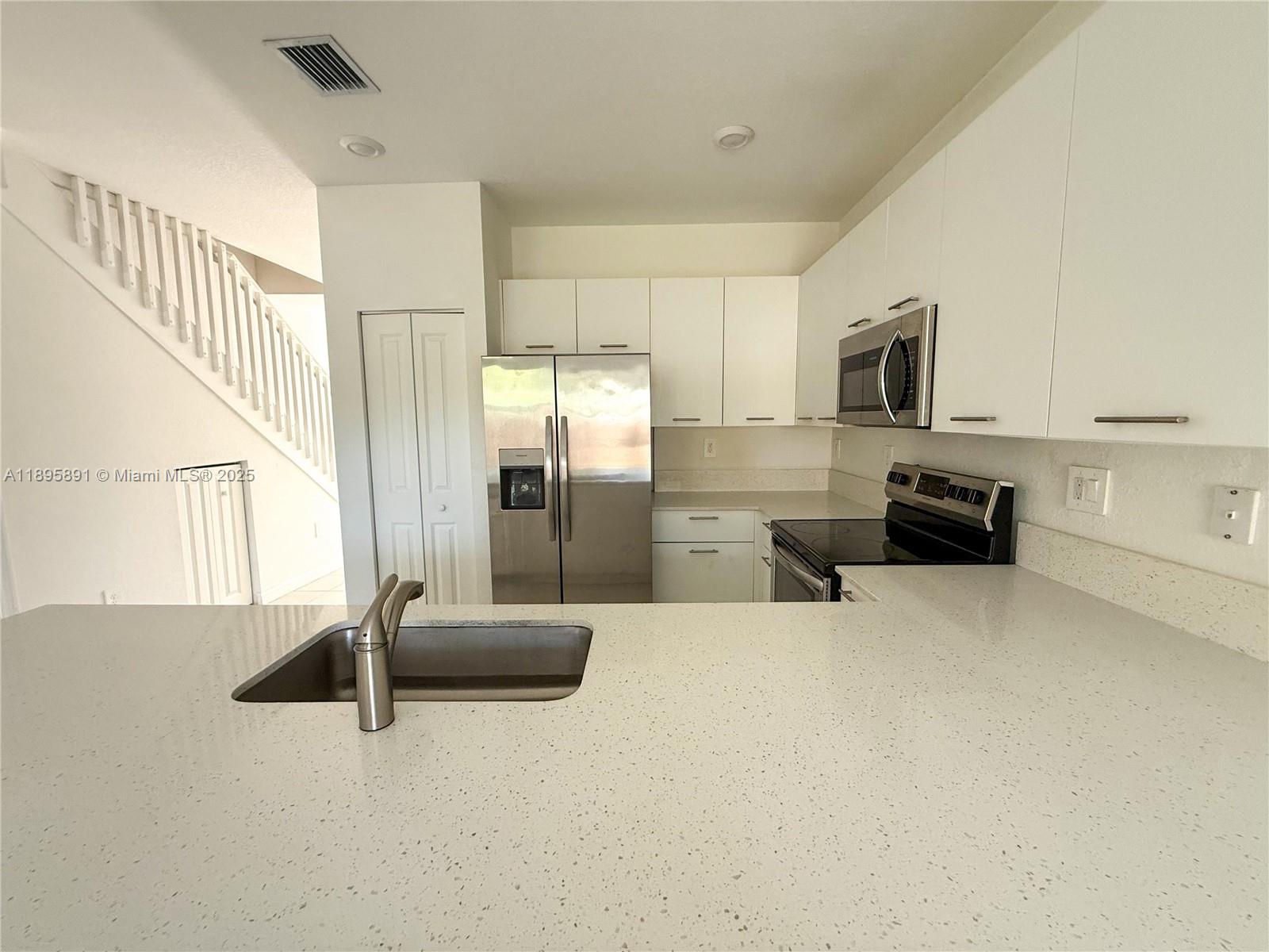 A kitchen features white cabinets, stainless steel appliances, and a light-colored quartz countertop — 12445 NW 23rd Ct, Miami FL 33167, MIAMI, FL