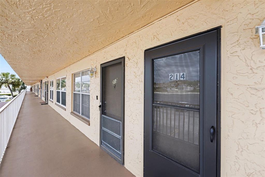 An exterior walkway features a row of apartment doors with screen doors and windows — 6400 46TH AVENUE N UNIT 214, KENNETH CITY, FL