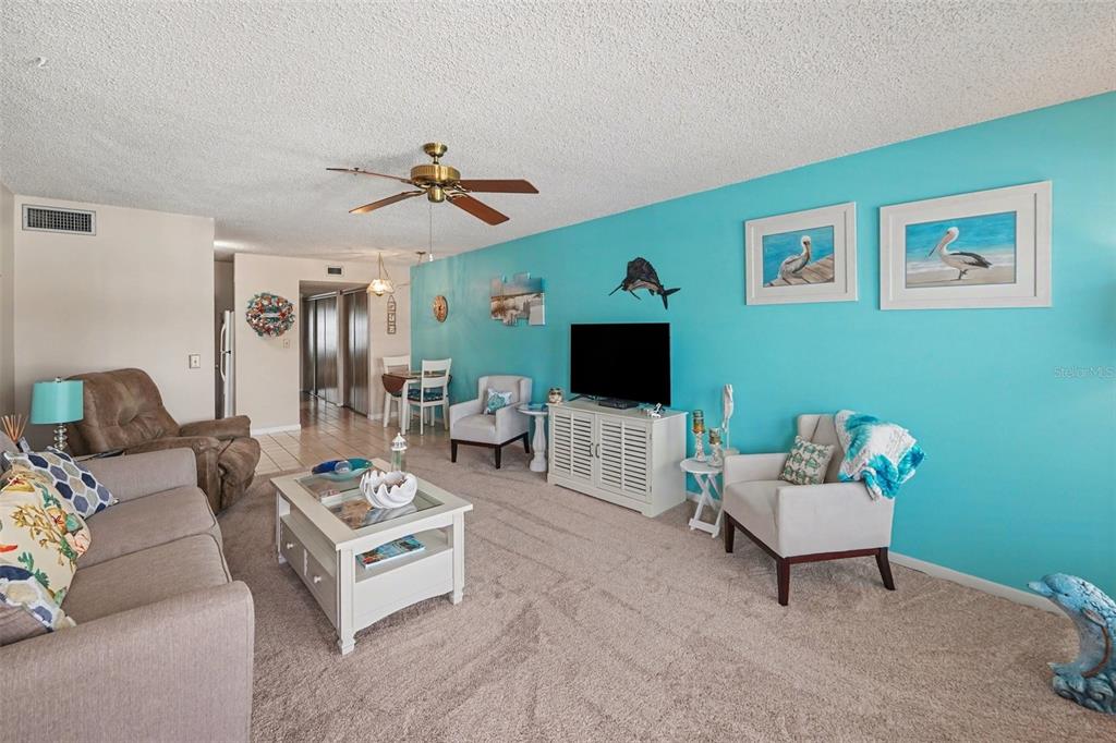 A living room features a bright blue accent wall, beige carpet, and coastal-themed decor — 6400 46TH AVENUE N UNIT 214, KENNETH CITY, FL