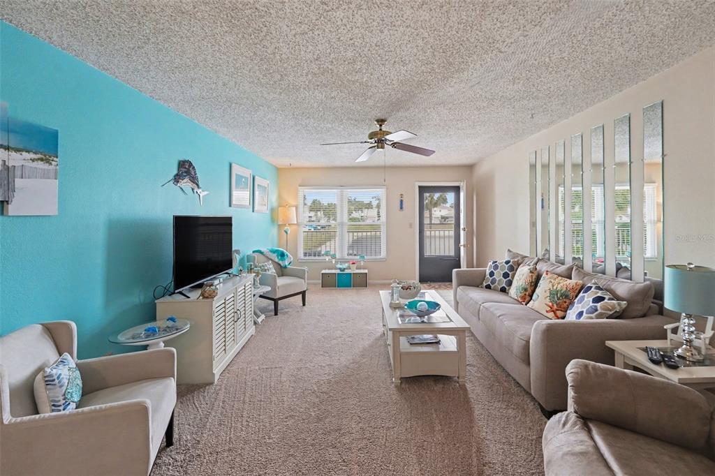 A living room features a turquoise accent wall, beige carpet, a sofa, and mirrored panels — 6400 46TH AVENUE N UNIT 214, KENNETH CITY, FL