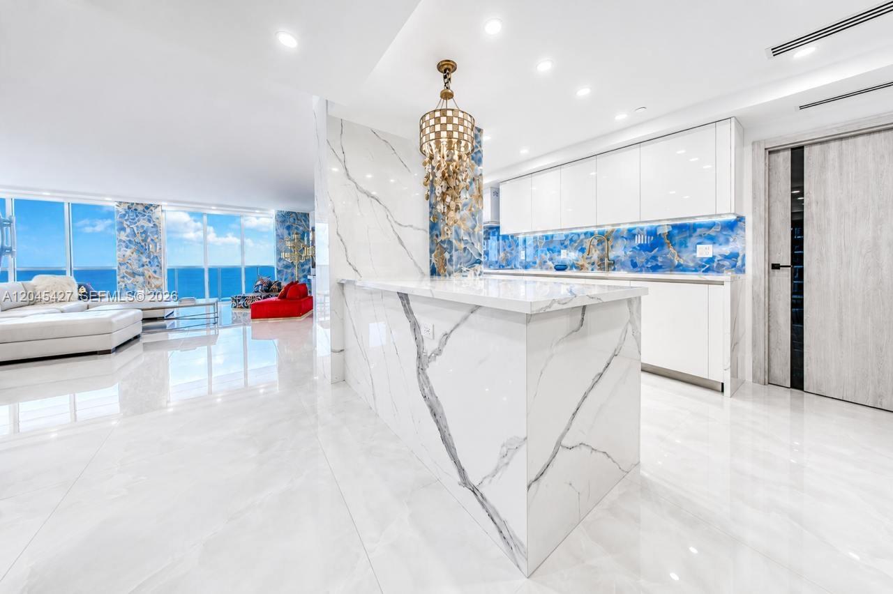 A modern kitchen features a white marble waterfall island, white cabinetry, and a blue backsplash — 1800 S Ocean Dr # 3601, Hallandale Beach FL 33009, HALLANDALE BEACH, FL