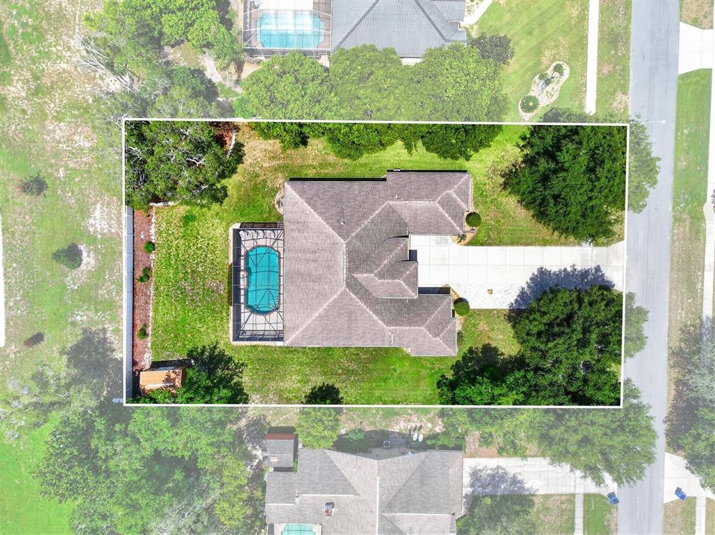 An aerial view shows a house with a pool enclosure, driveway, and surrounding trees — 12470 HUNTINGTON WOODS AVENUE, SPRING HILL, FL