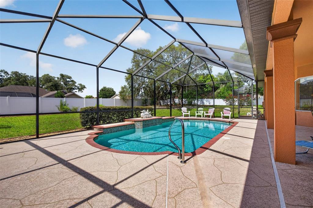 A swimming pool with a spillover spa is enclosed by a screen cage on a patio — 12470 HUNTINGTON WOODS AVENUE, SPRING HILL, FL