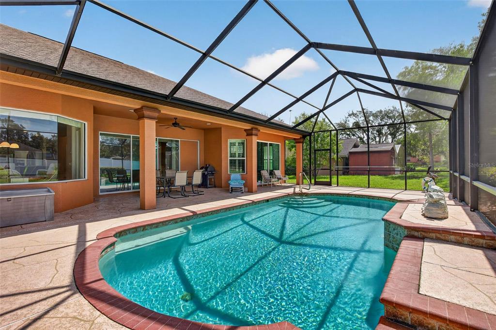 A swimming pool with a brick-trimmed edge sits inside a screened-in patio area — 12470 HUNTINGTON WOODS AVENUE, SPRING HILL, FL