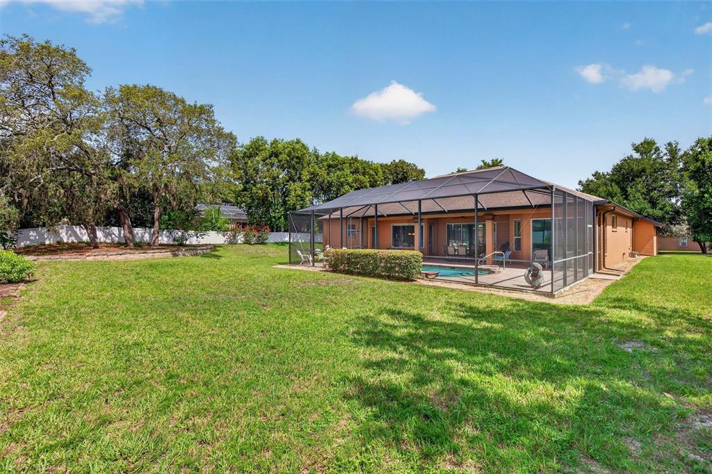 A backyard features a screened-in pool enclosure attached to the rear of a house — 12470 HUNTINGTON WOODS AVENUE, SPRING HILL, FL