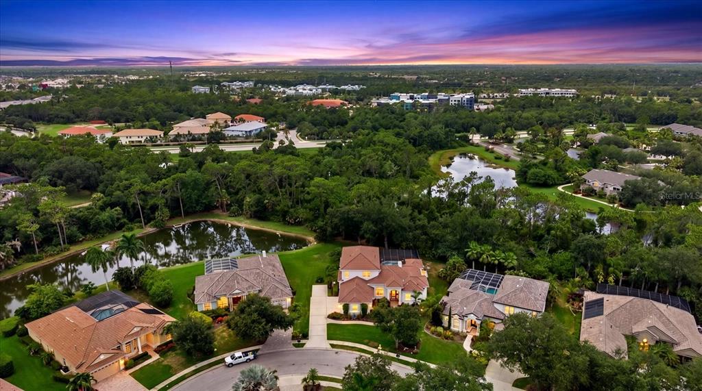 An aerial view shows several suburban houses with pools surrounded by trees and small ponds — 7574 TORI WAY, BRADENTON, FL