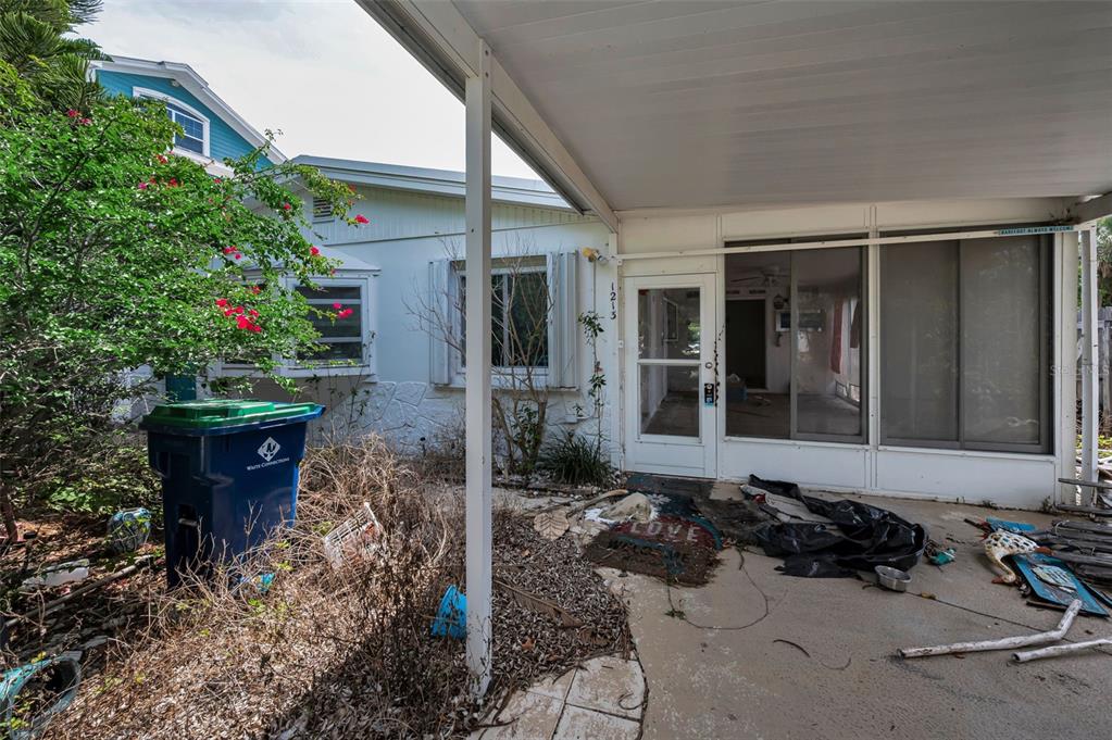 A covered patio area features a white door, sliding glass windows, and a blue trash bin — 1213 BAY PALM BOULEVARD, INDIAN ROCKS BEACH, FL